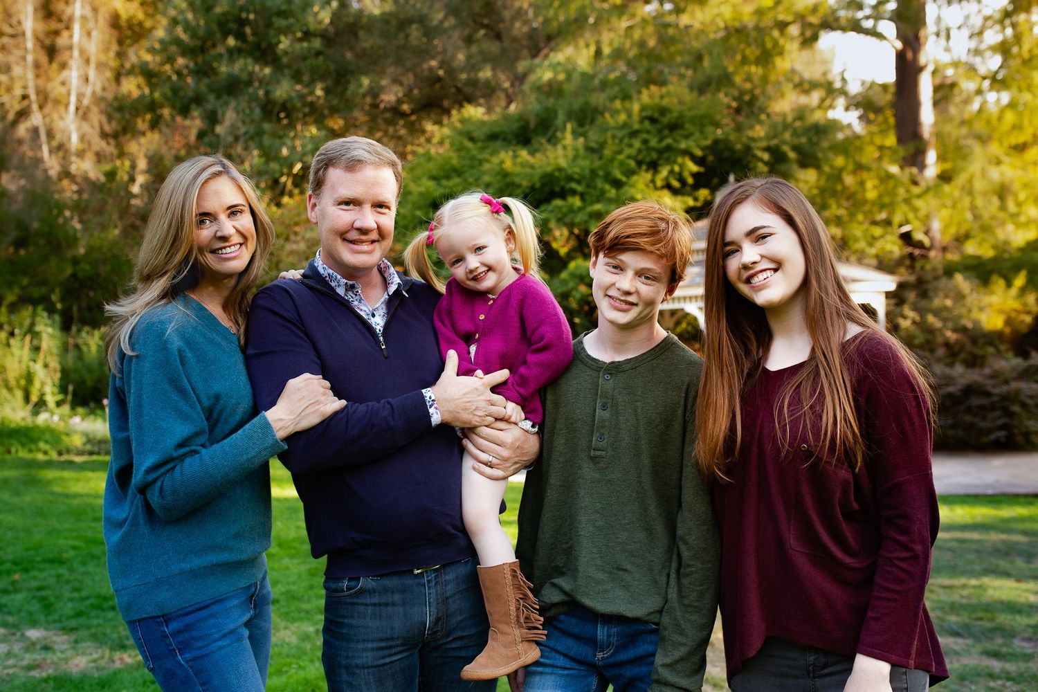 A family poses together outdoors in coordinated fall outfits with autumn foliage in the background.