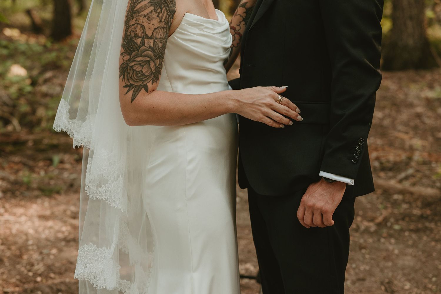 A wedding couple stands together at sunset against a backdrop of evergreen trees.