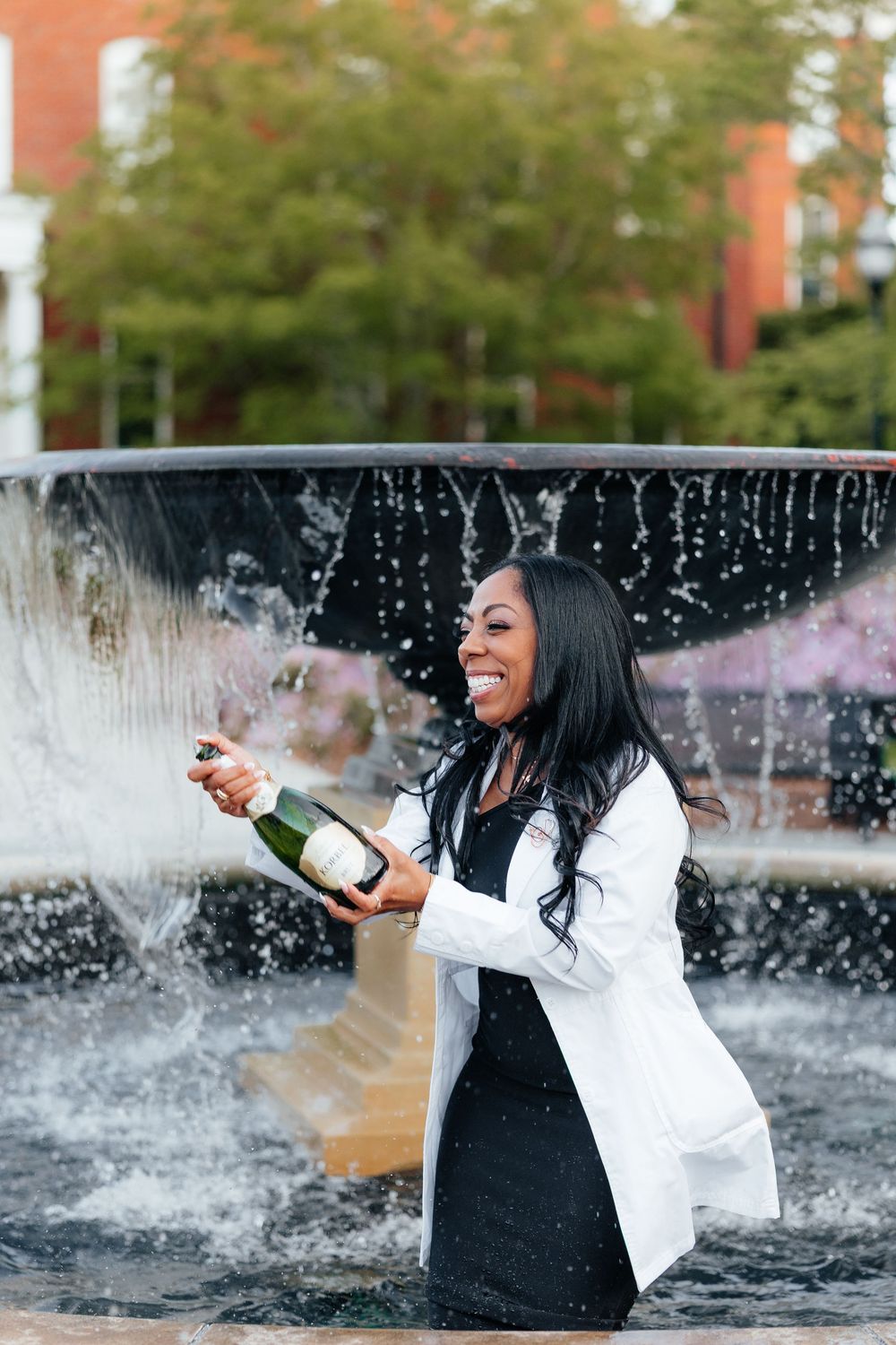 A person in black and white attire celebrates with champagne spray near a fountain, creating a joyful moment.