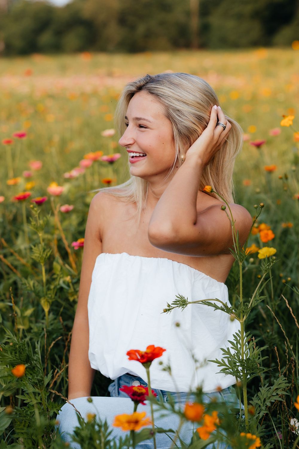 A person in a white top sits among vibrant orange and yellow wildflowers in a summer meadow, smiling joyfully.
