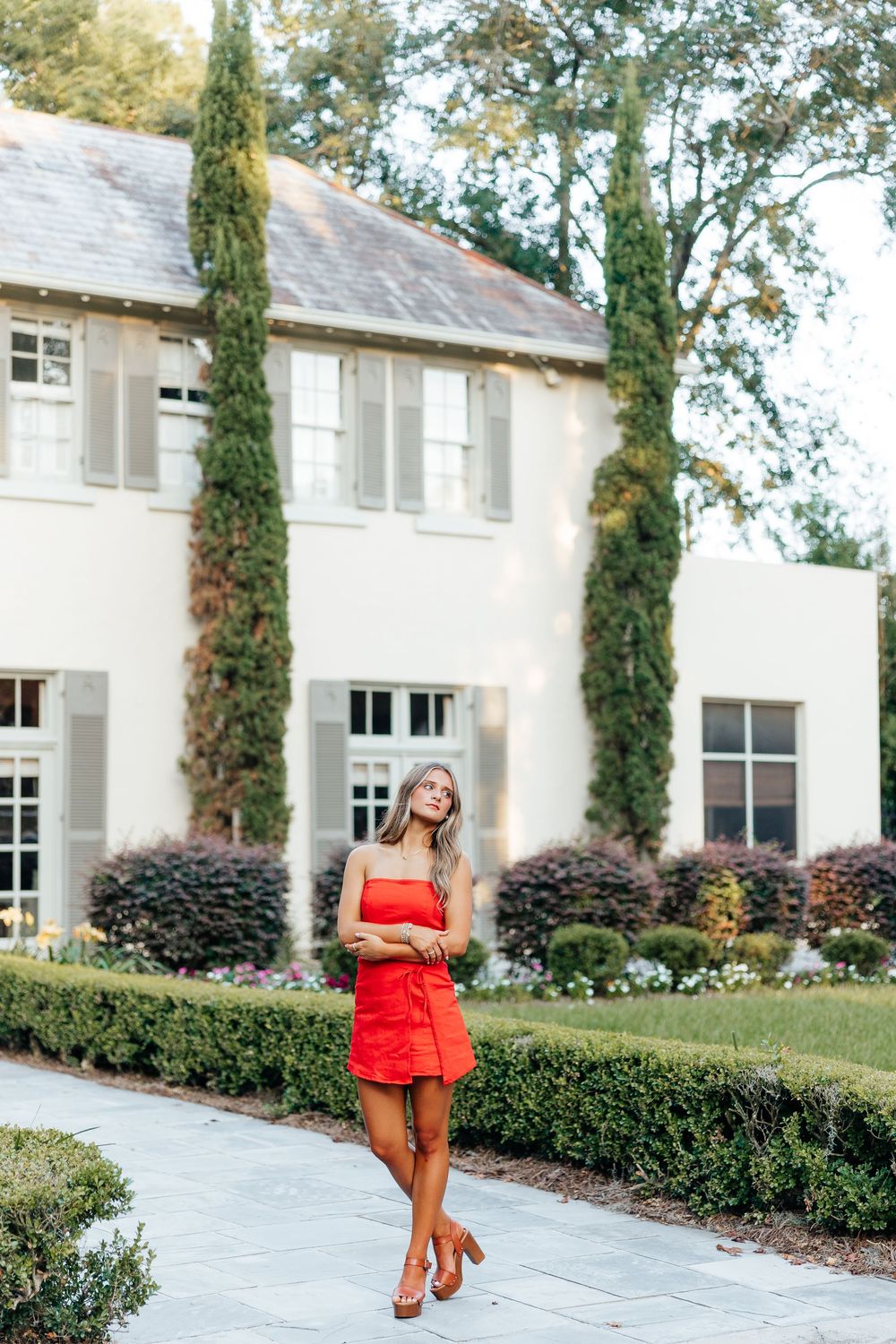 Elegant white house exterior with tall cypress trees and manicured hedges features a curved walkway and classic architecture.