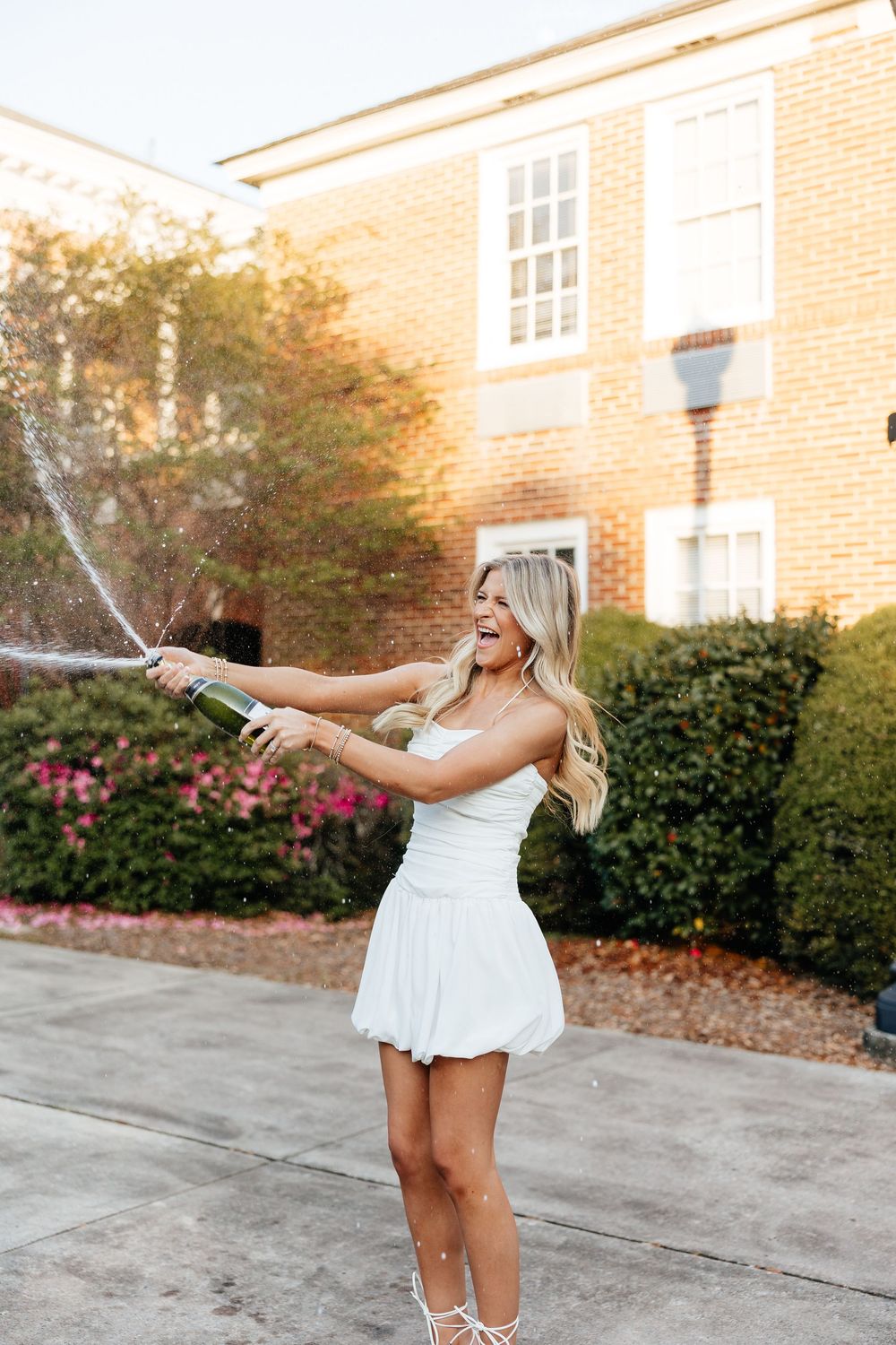 A sequence of joyful moments in white dresses with champagne bottles on a brick building backdrop.