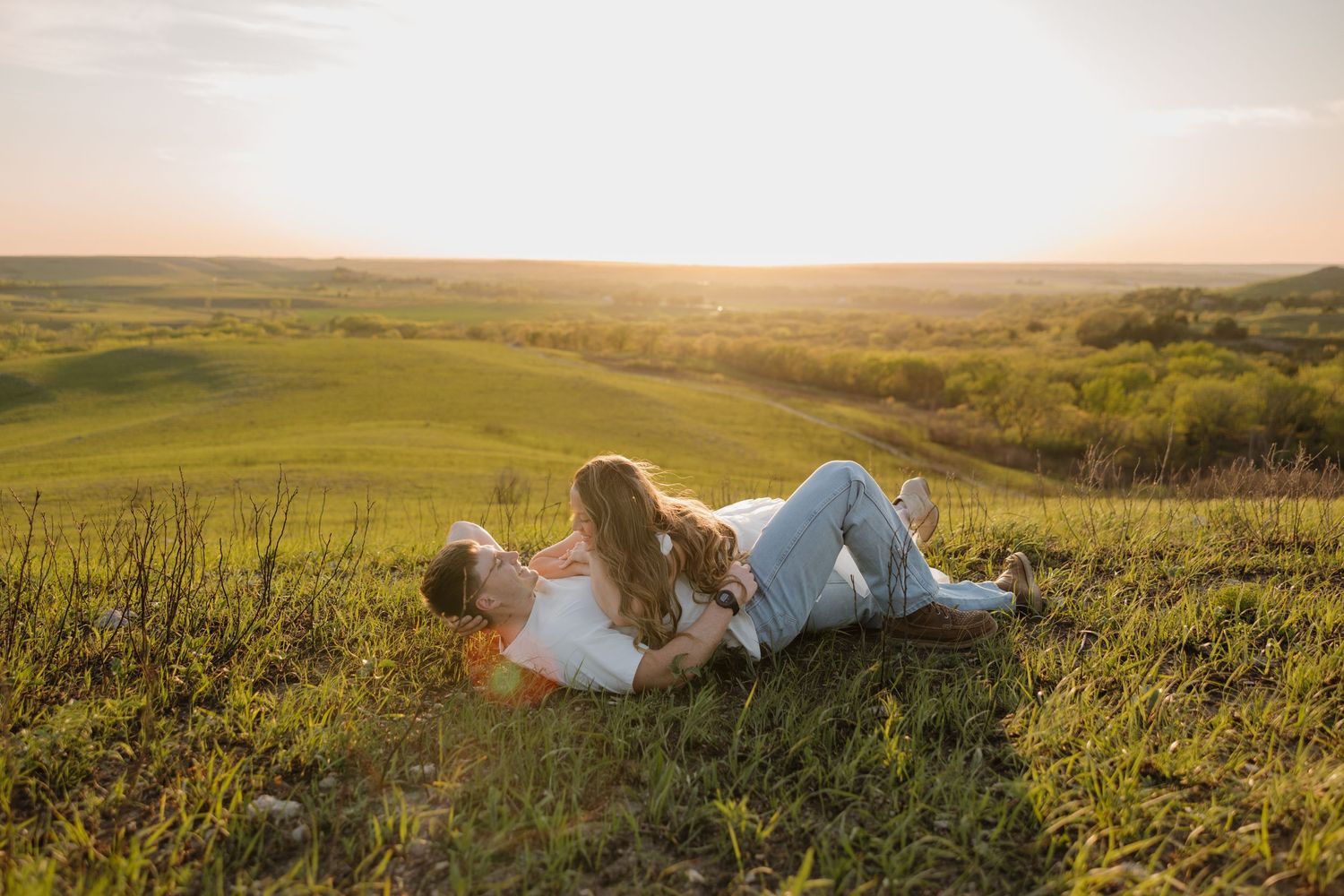 Couple relaxing together on grassy hillside during golden hour sunset.