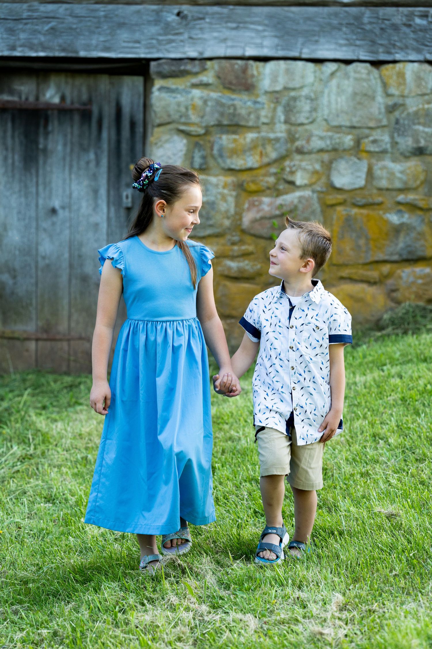 Young figures in bright clothing standing together near a rustic stone wall and wooden structure.