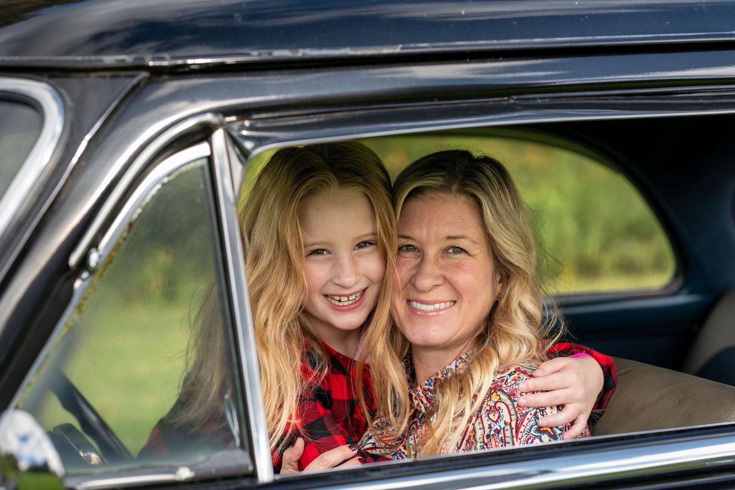 Two people sharing a joyful moment while sitting in a classic car on a sunny day.