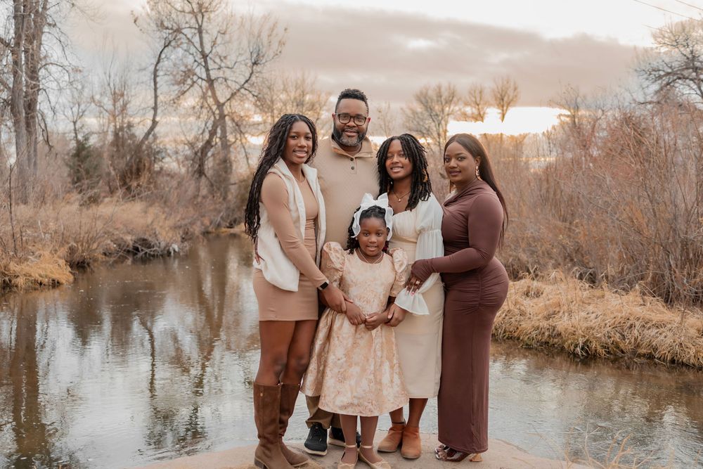 Family of five posing together near a serene river during golden hour in a scenic outdoor setting.