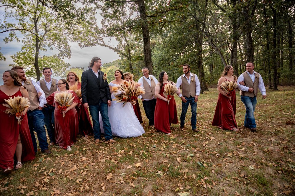 Wedding party in burgundy and casual attire poses on autumn hillside.
