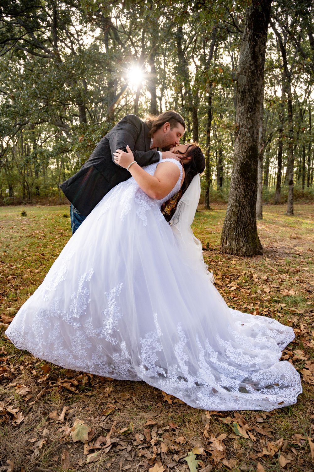 Romantic dip pose in white wedding dress against autumn forest backdrop.