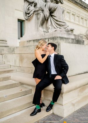A romantic couple in formal attire posing on stone steps showing playful affection.