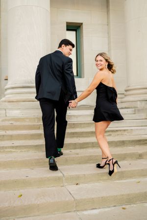 A stylish couple in formal wear playing and posing on architectural steps.