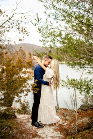 A romantic photoshoot by a lake with autumn foliage in the background.
