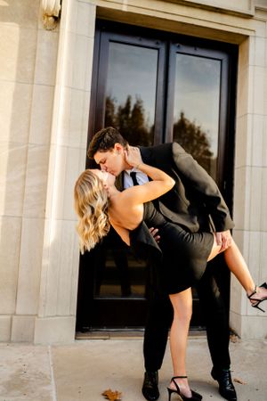 A couple in formal attire sharing a romantic dip pose against a stone building.