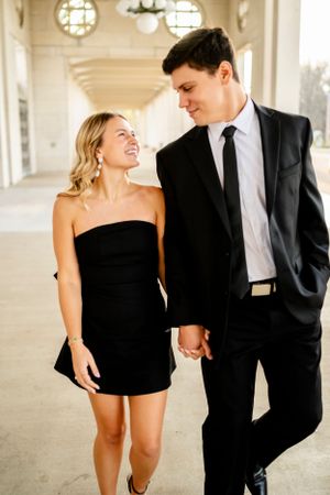 An elegant couple in formal wear poses playfully in an architectural setting.