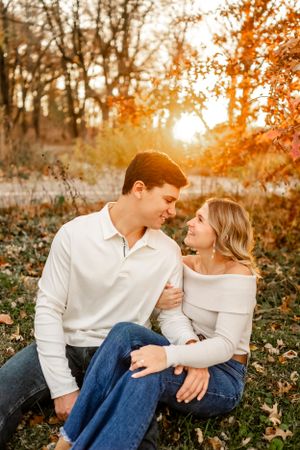 Couple in matching white tops share tender moments among fall foliage at sunset.