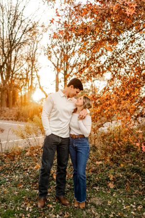 Couple in casual attire share playful moments against a backdrop of autumn trees.