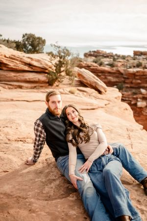 Couple relaxing together on red sandstone rocks in casual outdoor attire.