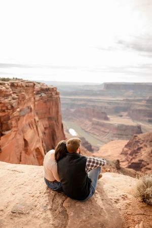Two people lying on the edge of a dramatic canyon overlook with vast desert views.