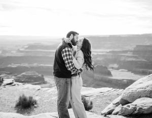 Black and white photo of couple sharing tender moment on desert canyon overlook.