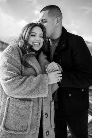 A romantic winter photoshoot showing a couple embracing while wearing cozy outerwear in black and white.