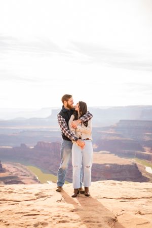 Wide landscape shot of couple sharing intimate moment on desert canyon overlook.