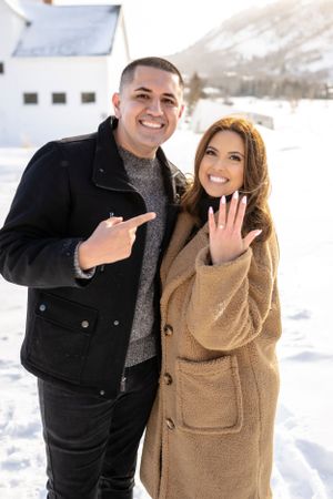 A playful winter engagement session with a couple laughing in the snow against a mountain backdrop.