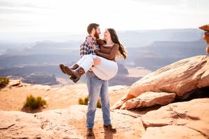 Couple shares romantic moments on red rock cliffs overlooking a scenic desert canyon landscape.