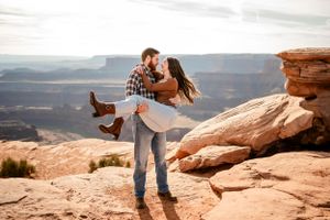 Playful couple posing on dramatic red rock formations in desert landscape.