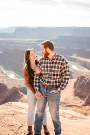 Couple sharing lighthearted moment on cliff edge with vast canyon views.