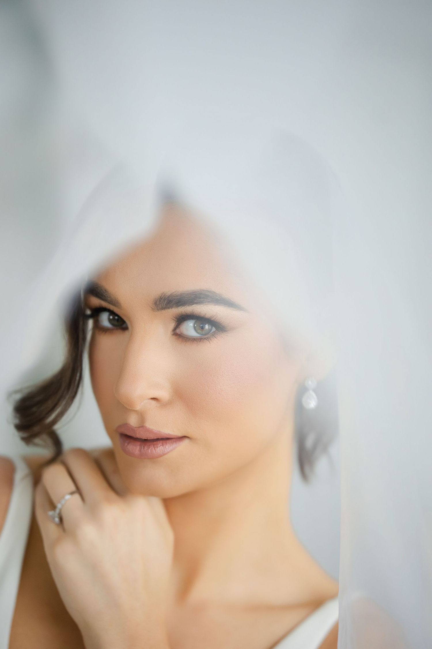 Close-up beauty shot with soft focus showing delicate makeup details through a white veil.