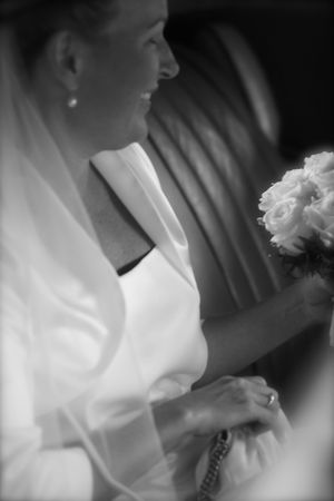 Black and white portrait of a bride in white dress and shawl holding a bouquet of roses.