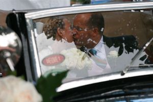 A vintage wedding day scene showing a decorated black car with a couple in formal attire visible through the window.