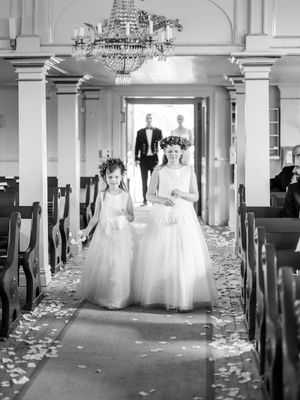 An elegant indoor wedding ceremony aisle with white rose petals scattered on the floor and crystal chandeliers overhead.