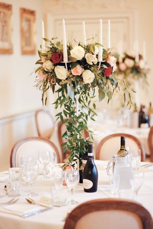 Elegant wedding table centerpiece with white and red roses, candles and eucalyptus in a navy blue vase.