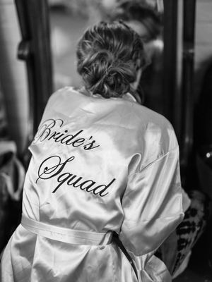Back view of someone wearing a white satin robe with 'Bride's Squad' text in cursive lettering.