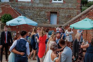 Wedding guests socializing and celebrating under blue umbrellas outside a rustic brick building.