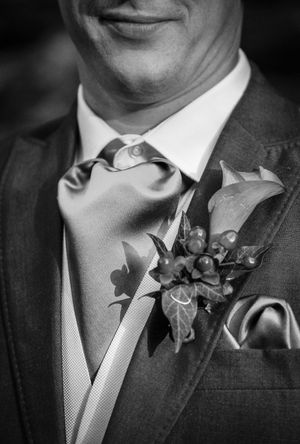 A black and white wedding photo detail showing a groom's boutonniere and tie against a dark suit.