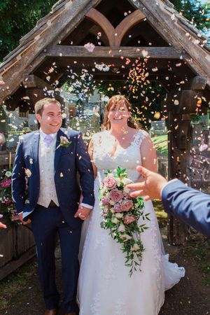 Wedding couple celebrating under wooden gazebo as confetti showers down during outdoor ceremony.