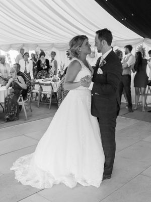 A couple dances at a wedding reception under a white tent with guests watching in the background.