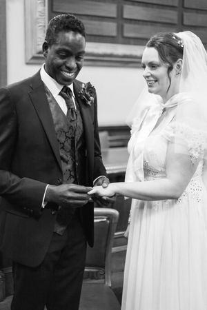 A joyful wedding ceremony moment in black and white as the couple exchanges rings.