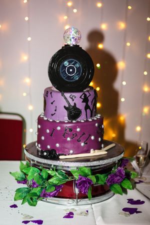 A purple disco-themed wedding cake decorated with vinyl records and sparkly lights in the background.