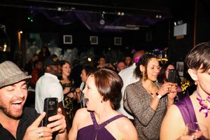 Crowd of people dancing and socializing in a dimly lit nightclub venue with black walls.