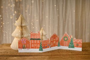 Festive paper craft display featuring colorful houses and honeycomb trees with holiday lighting.