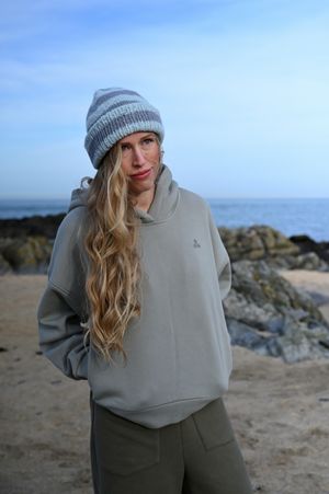 Coastal fashion scene with grey hoodie and striped beanie against ocean backdrop.