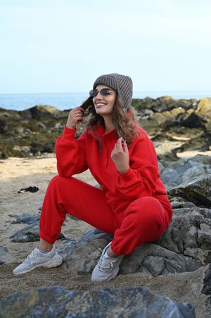 Casual outdoor portrait in red tracksuit and beanie on rocky beach landscape.