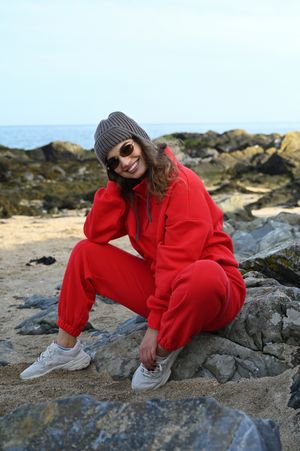 Energetic pose in bright red tracksuit on coastal rocks during sunset.