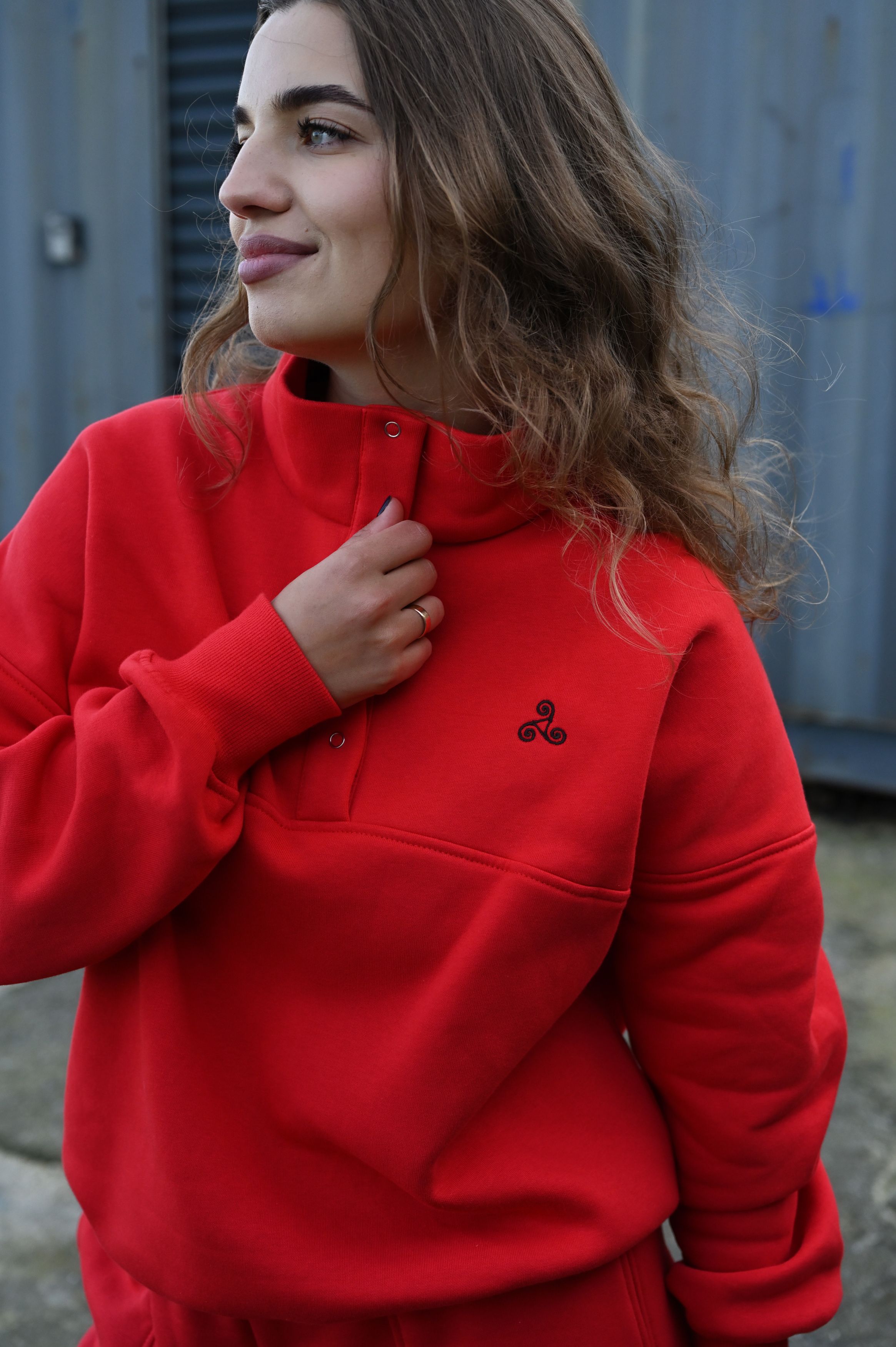 Stylish portrait in a vibrant red sweatshirt against an industrial backdrop.