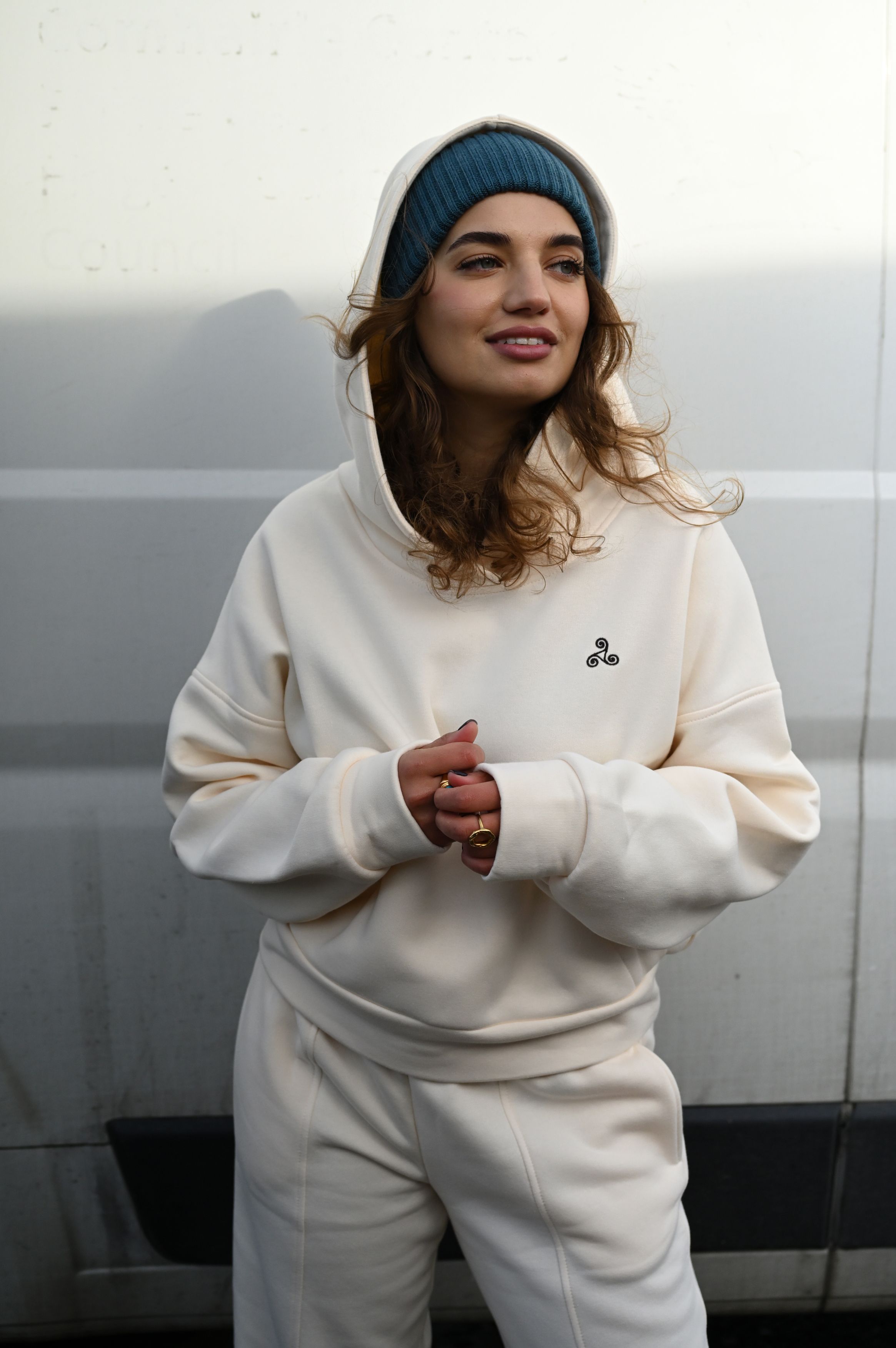 Person wearing cream-colored hoodie and navy beanie smiling against gray background.