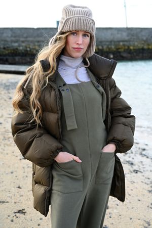 Casual winter outfit featuring khaki overalls and beige beanie on a beach.