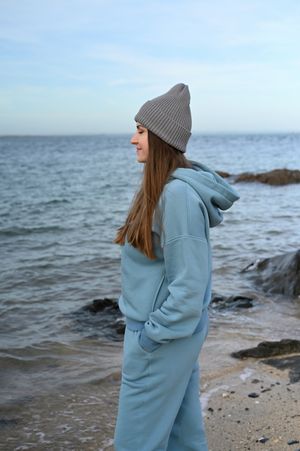 Person in pale blue jumpsuit and gray beanie looking out at the ocean.