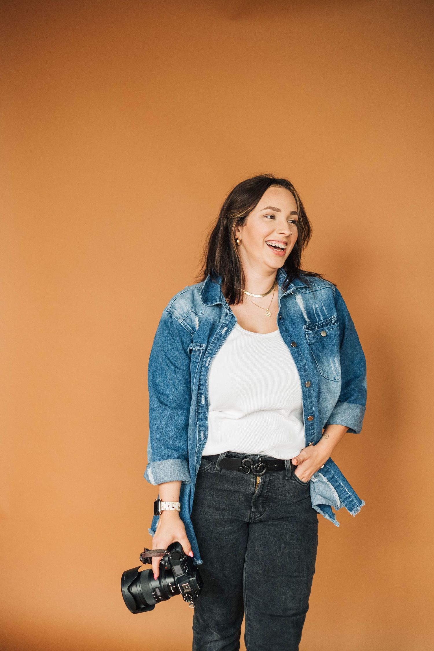 Person in denim jacket holding camera against orange background.